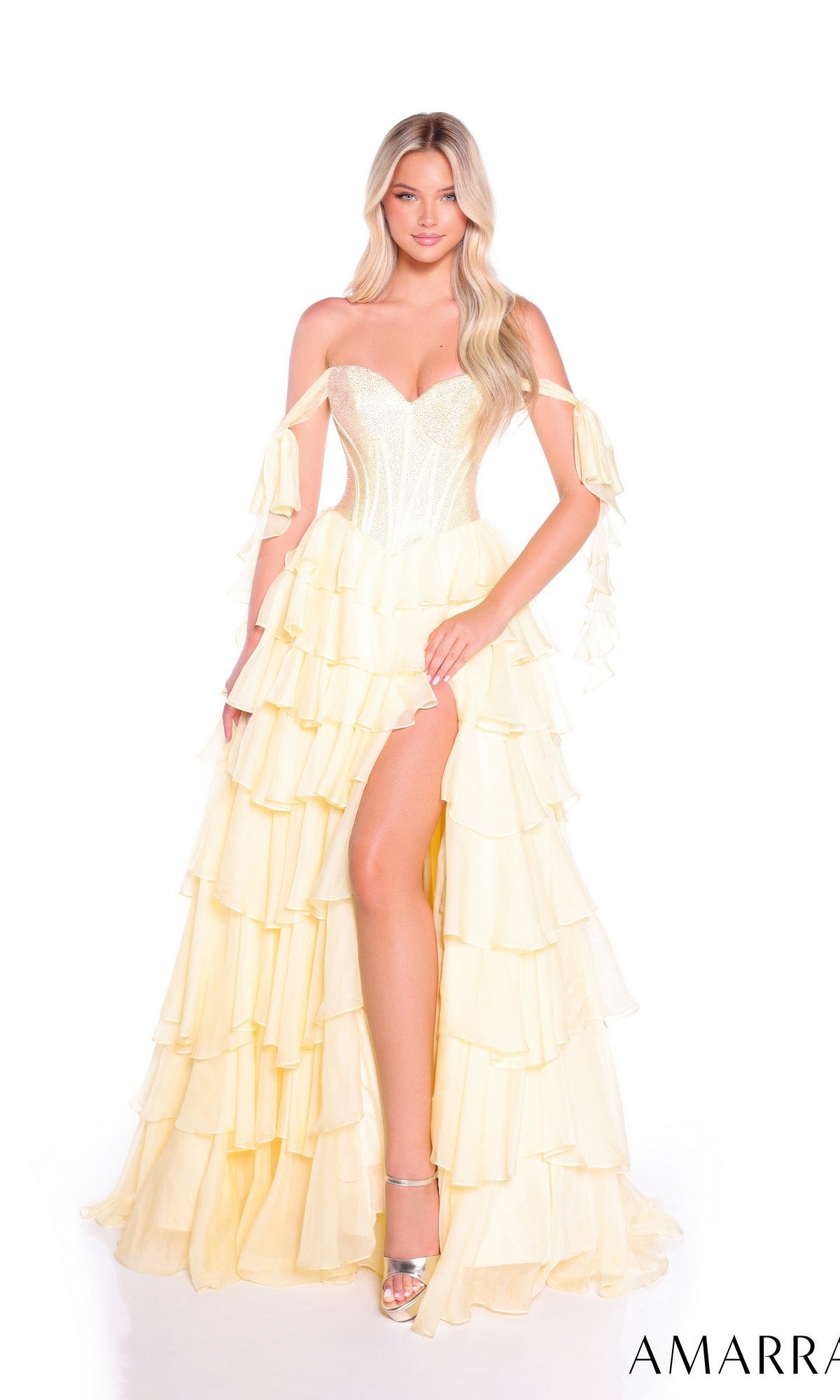 A woman in the Amarra 89285 long prom dress, featuring an off-the-shoulder design, tiered chiffon skirt, and thigh-high slit, paired with metallic high heels, stands against a white background.